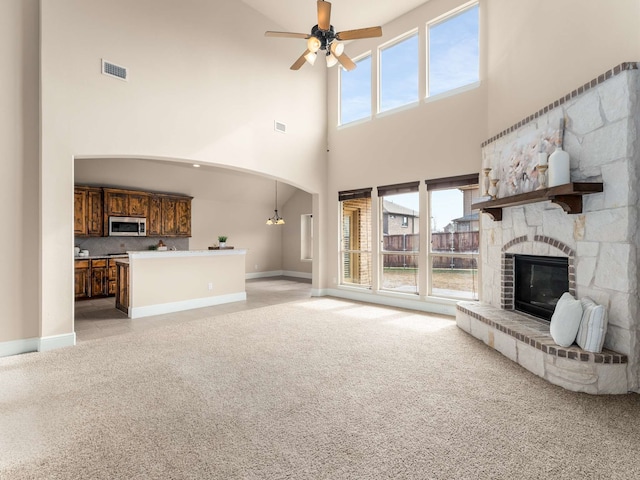 unfurnished living room featuring ceiling fan with notable chandelier, light carpet, a stone fireplace, and a towering ceiling