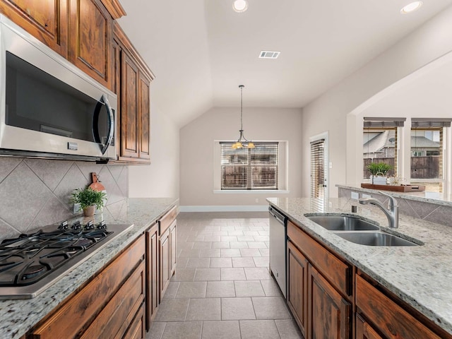 kitchen with sink, backsplash, hanging light fixtures, stainless steel appliances, and light stone countertops