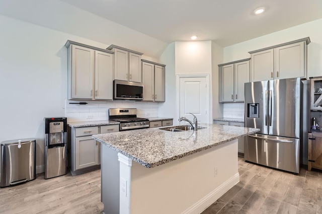 kitchen with sink, light stone counters, light hardwood / wood-style flooring, appliances with stainless steel finishes, and an island with sink