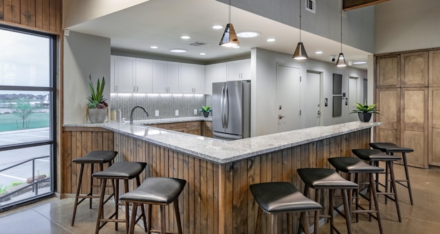 kitchen featuring pendant lighting, stainless steel refrigerator, white cabinetry, decorative backsplash, and kitchen peninsula