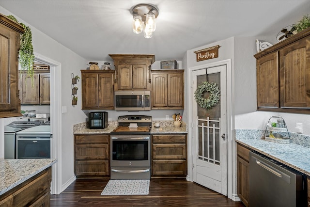 kitchen featuring light stone countertops, appliances with stainless steel finishes, dark hardwood / wood-style floors, and washing machine and clothes dryer