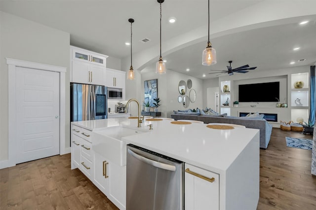 kitchen with appliances with stainless steel finishes, white cabinetry, sink, pendant lighting, and an island with sink