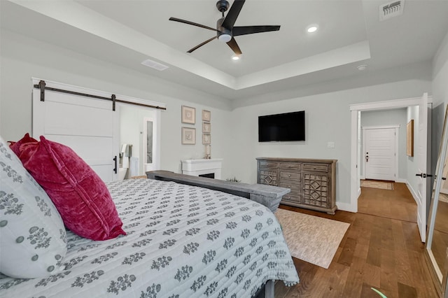 bedroom featuring a barn door, ceiling fan, a raised ceiling, and dark hardwood / wood-style flooring