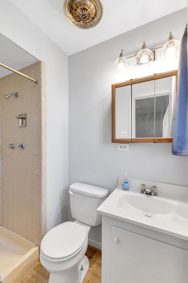 bathroom with vanity, toilet, hardwood / wood-style floors, and a tile shower