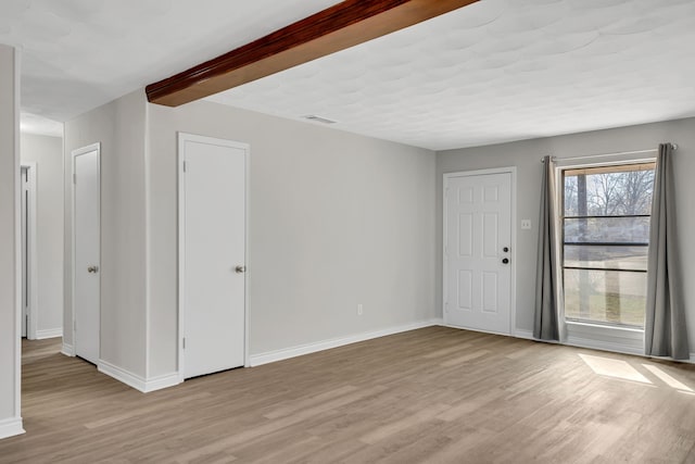 spare room featuring beamed ceiling and light hardwood / wood-style flooring