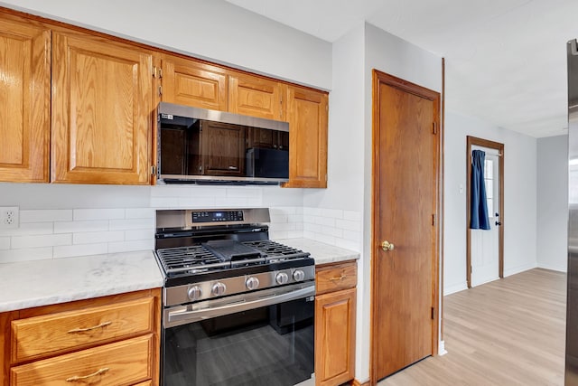 kitchen featuring stainless steel gas range oven, decorative backsplash, light wood-type flooring, and light stone countertops