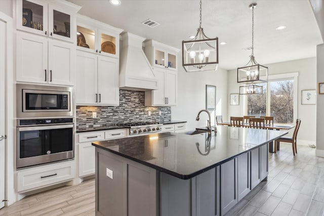 kitchen with custom exhaust hood, tasteful backsplash, a notable chandelier, a sink, and stainless steel appliances