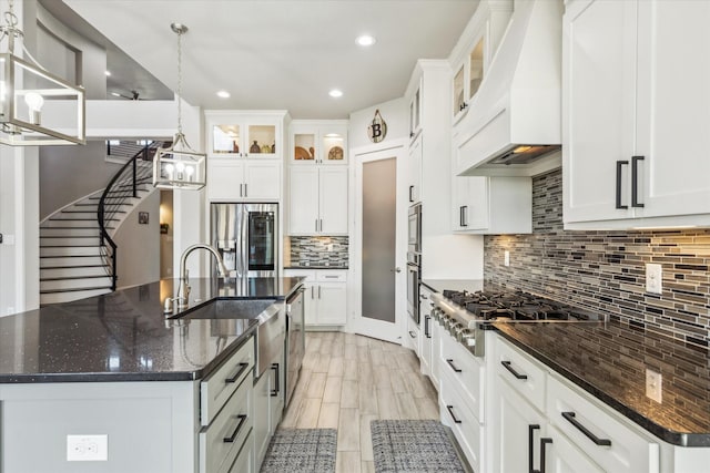 kitchen with an island with sink, premium range hood, white cabinets, decorative backsplash, and appliances with stainless steel finishes
