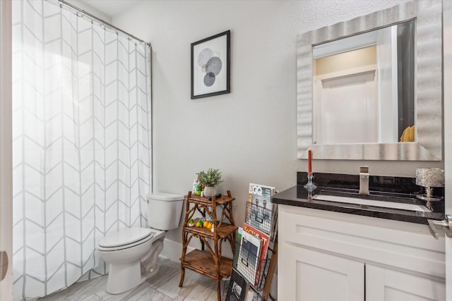 full bathroom featuring vanity, toilet, curtained shower, a textured wall, and baseboards
