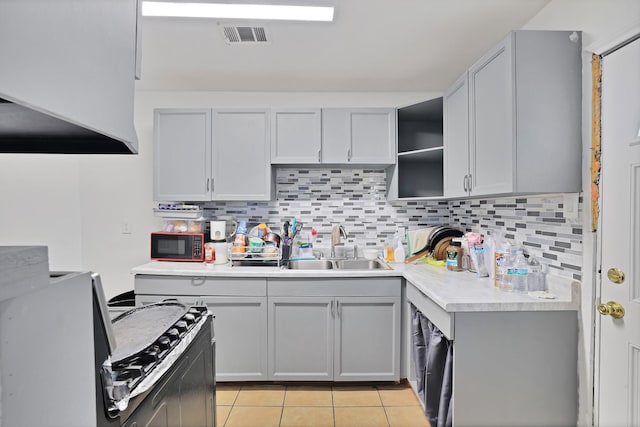 kitchen featuring sink, backsplash, gray cabinetry, light tile patterned floors, and range