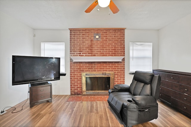 living room with a fireplace, light wood-type flooring, a textured ceiling, and ceiling fan