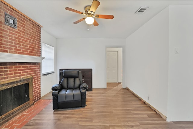 living area featuring ceiling fan, light hardwood / wood-style floors, and a brick fireplace