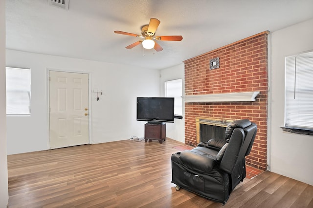 sitting room featuring ceiling fan, a brick fireplace, hardwood / wood-style floors, and a textured ceiling