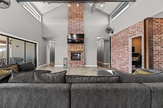 living room featuring a fireplace, rail lighting, a high ceiling, and brick wall