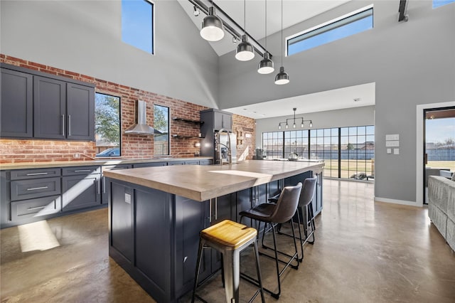 kitchen with hanging light fixtures, wooden counters, a high ceiling, a kitchen bar, and a kitchen island with sink