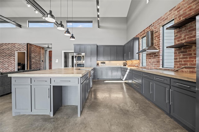 kitchen with brick wall, wall chimney exhaust hood, a towering ceiling, concrete floors, and gray cabinets