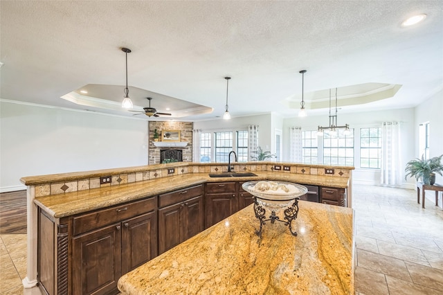 10545 Lago Vis, Quinlan, TX 75474 - kitchen featuring a tray ceiling, a stone fireplace, baseboards, a sink, and a ceiling fan