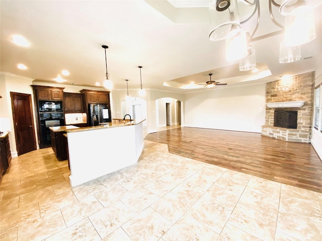 kitchen with a large island, decorative light fixtures, ceiling fan, a fireplace, and black appliances