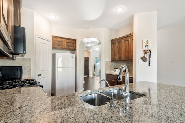 kitchen featuring light stone counters, sink, range, and white refrigerator