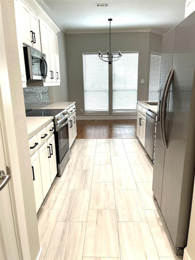 kitchen with crown molding, white cabinets, appliances with stainless steel finishes, a chandelier, and light countertops