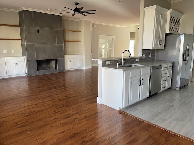 kitchen with appliances with stainless steel finishes, white cabinetry, sink, ornamental molding, and a tile fireplace