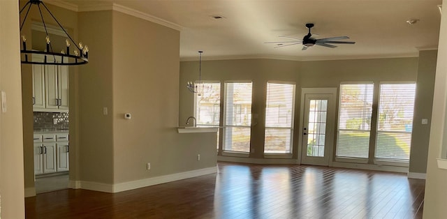 spare room with ceiling fan with notable chandelier, a healthy amount of sunlight, ornamental molding, and dark hardwood / wood-style flooring