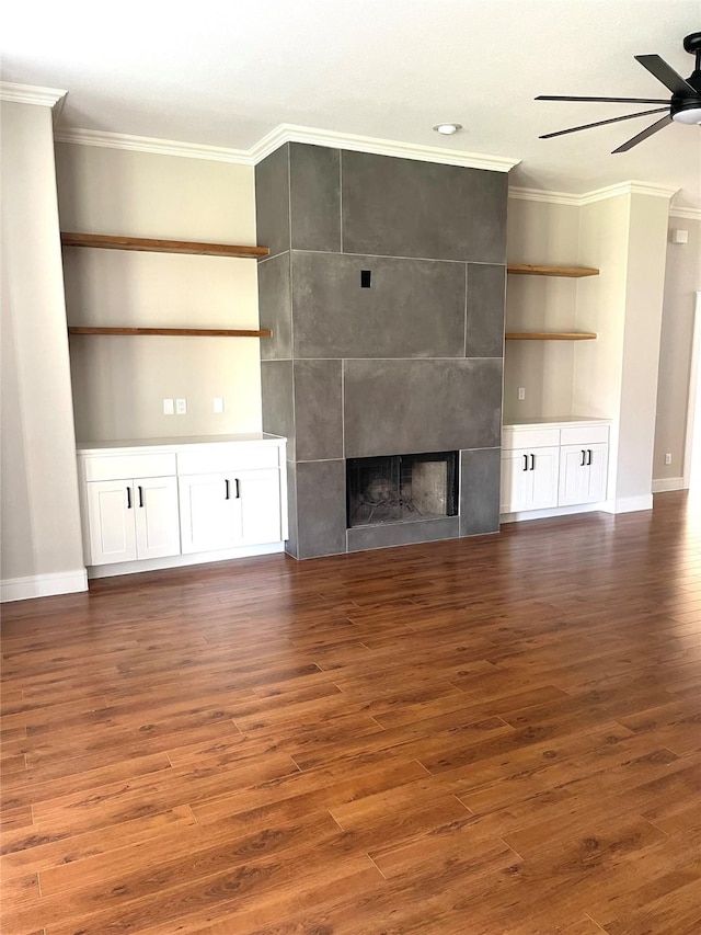 unfurnished living room with a fireplace, ornamental molding, dark hardwood / wood-style flooring, built in features, and ceiling fan