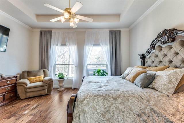 bedroom with ceiling fan, a raised ceiling, crown molding, and wood-type flooring