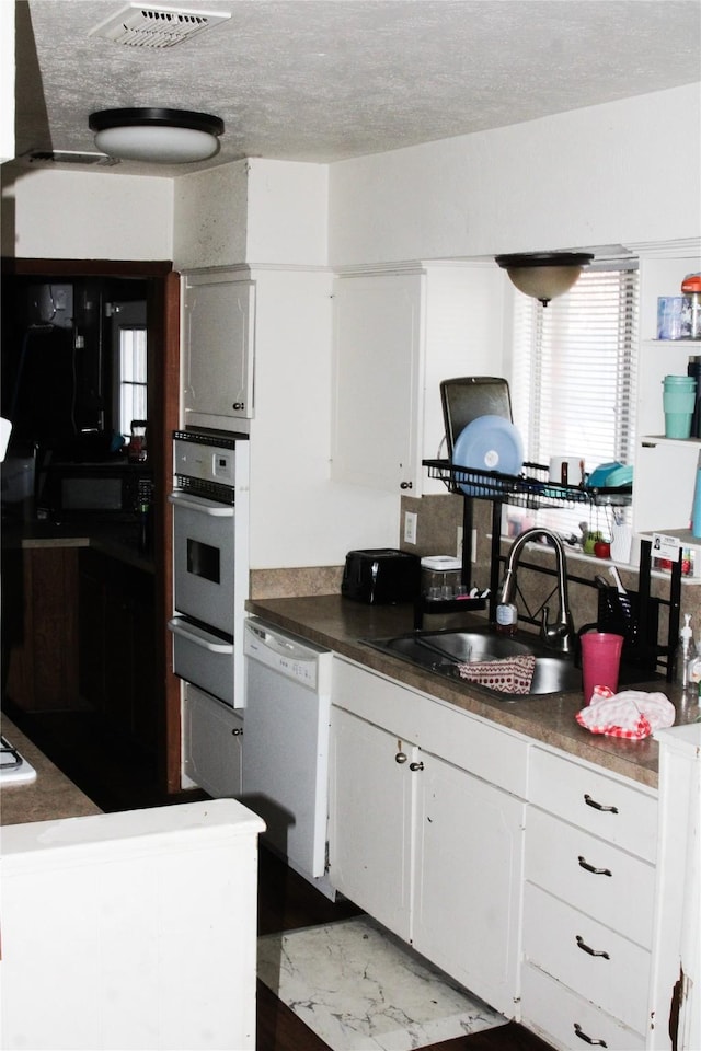 kitchen with a textured ceiling, white cabinetry, sink, stainless steel oven, and white dishwasher