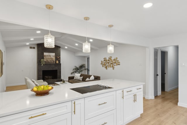 kitchen with white cabinetry, black electric stovetop, vaulted ceiling with beams, hanging light fixtures, and a large fireplace