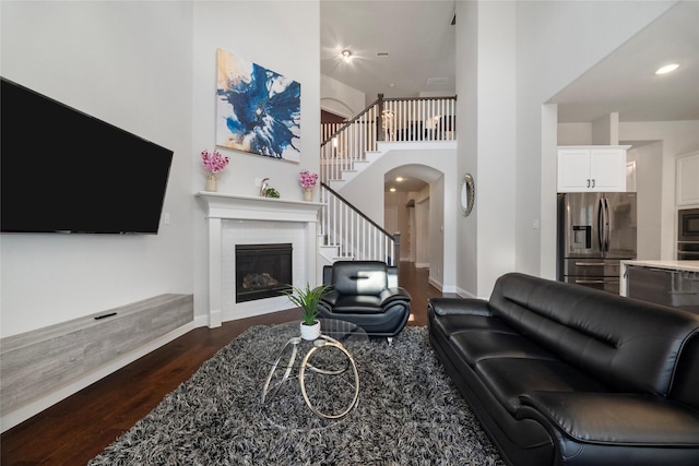 living room featuring baseboards, arched walkways, a glass covered fireplace, dark wood-style flooring, and stairs