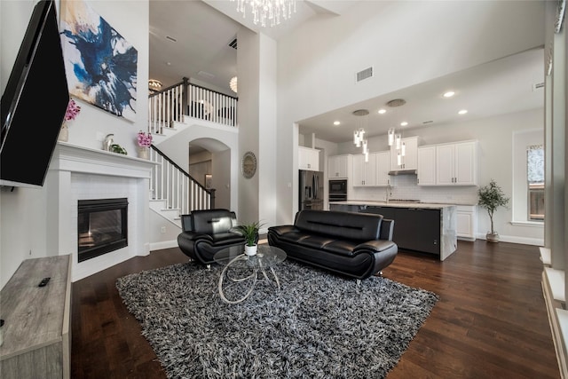 living room featuring visible vents, baseboards, stairs, dark wood-style floors, and a glass covered fireplace