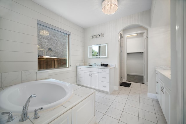 full bath featuring a sink, a spacious closet, two vanities, and a bath