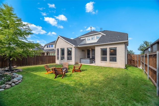 rear view of property featuring an outdoor fire pit, a fenced backyard, brick siding, a yard, and a hot tub