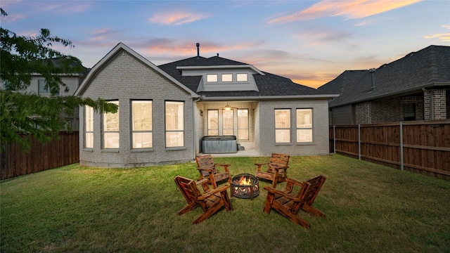 back of house at dusk featuring a yard, a fenced backyard, brick siding, and a fire pit