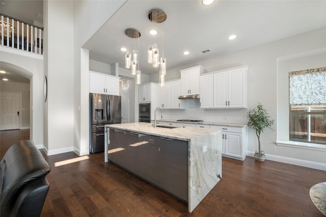 kitchen featuring a kitchen island with sink, stainless steel appliances, a sink, white cabinets, and hanging light fixtures