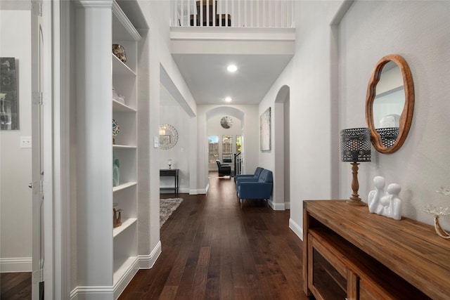 corridor featuring dark wood-style floors, baseboards, and arched walkways