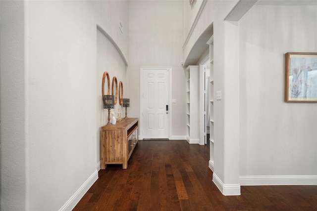 corridor featuring dark wood-style flooring, a high ceiling, and baseboards