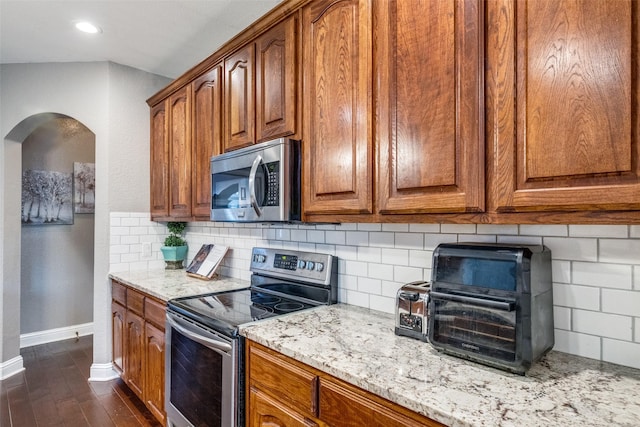 kitchen featuring light stone countertops, dark hardwood / wood-style floors, stainless steel appliances, and tasteful backsplash