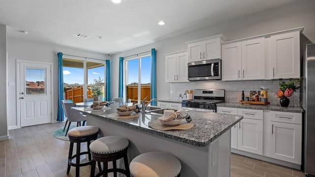 kitchen with white cabinets, backsplash, appliances with stainless steel finishes, and an island with sink