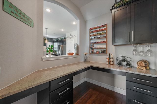 kitchen with dark wood-type flooring, stainless steel fridge, and light stone countertops