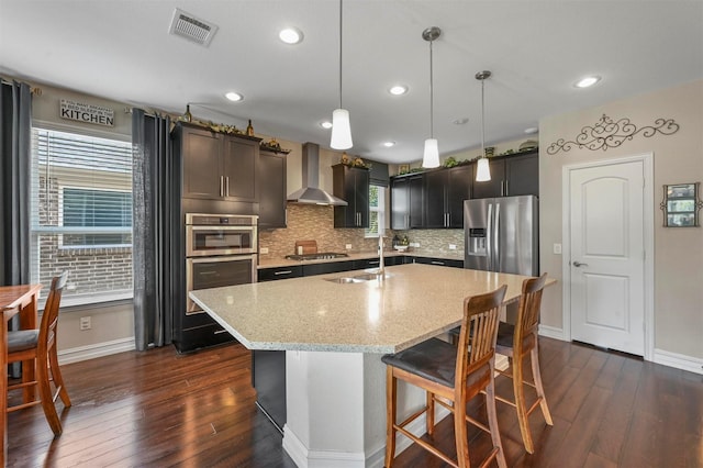 kitchen with light stone countertops, pendant lighting, wall chimney exhaust hood, stainless steel appliances, and sink