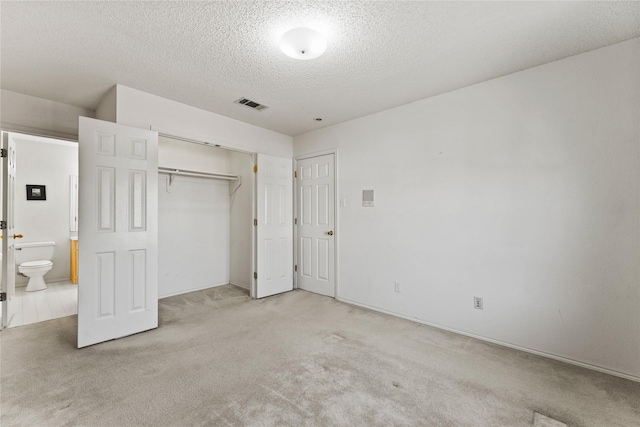 unfurnished bedroom with a closet, connected bathroom, light carpet, and a textured ceiling