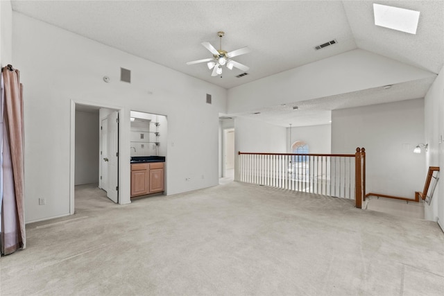 unfurnished living room with ceiling fan, vaulted ceiling with skylight, carpet floors, and a textured ceiling