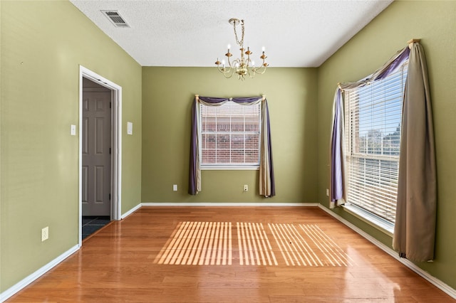 empty room featuring hardwood / wood-style flooring, a chandelier, and a textured ceiling