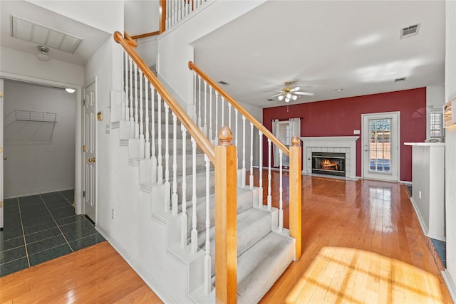 staircase featuring hardwood / wood-style floors, a fireplace, and ceiling fan