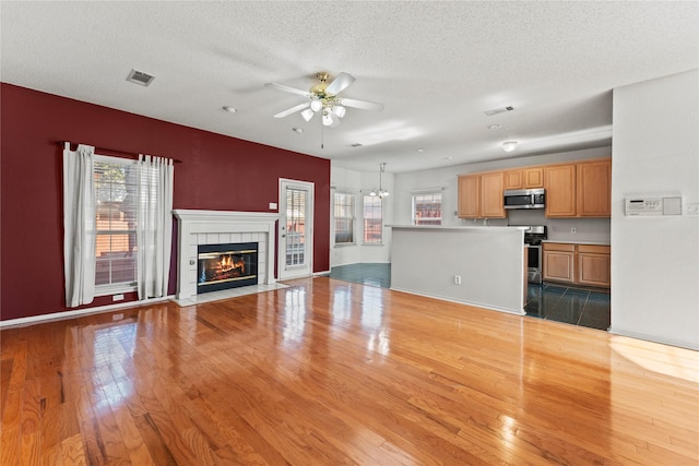 unfurnished living room with light hardwood / wood-style floors, plenty of natural light, a tiled fireplace, and ceiling fan with notable chandelier