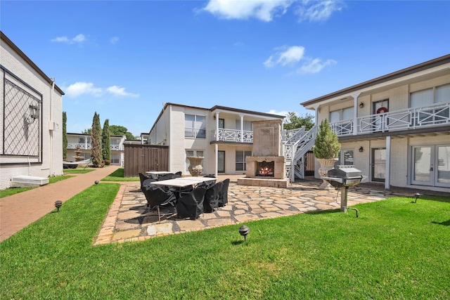 rear view of house featuring a yard, an outdoor stone fireplace, and a patio