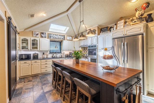 kitchen featuring butcher block countertops, stainless steel appliances, a center island, vaulted ceiling with skylight, and decorative backsplash