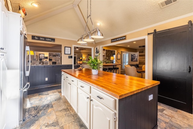 kitchen featuring a kitchen island, butcher block counters, white cabinets, hanging light fixtures, and a barn door